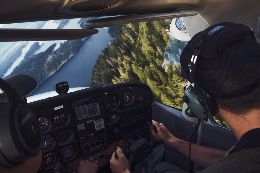 Pilot flying a small aircraft over a mountainous lake landscape, representing Business aircraft, leasing a business jet, business aircraft leasing, private aircraft loans, and the Falcon 8x as aviation financing and ownership options.